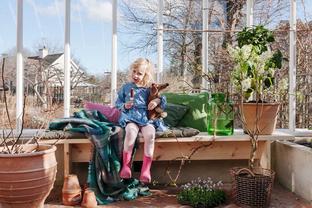 En flicka på en bänk omgiven av växter i växthus.
