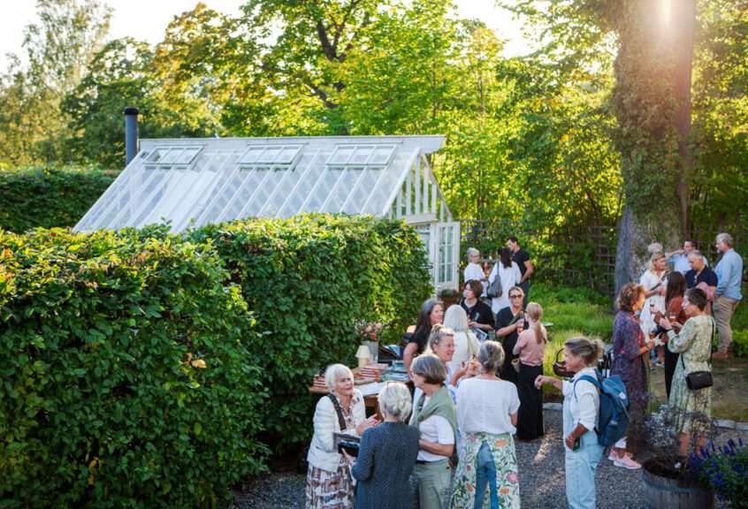 Folk i trädgård framför växthus.